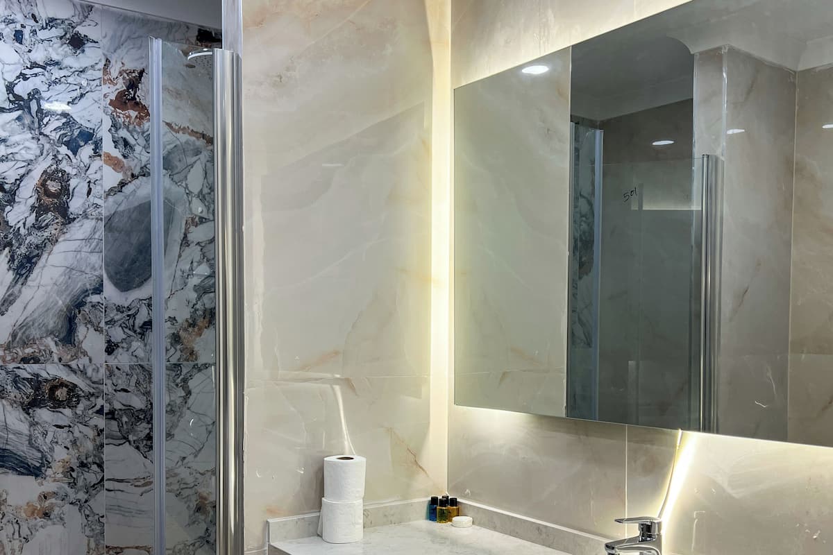 A modern bathroom with a marble vanity, a glass shower enclosure, and a large mirror.
