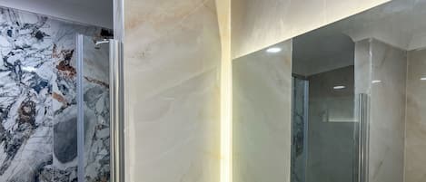 Un baño moderno con tocador de mármol, cabina de ducha con mampara de vidrio y un espejo grande.