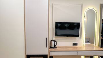 A modern hotel room with a bed, a desk with a flat-screen TV, a mini-fridge, and a mirror with LED lights.