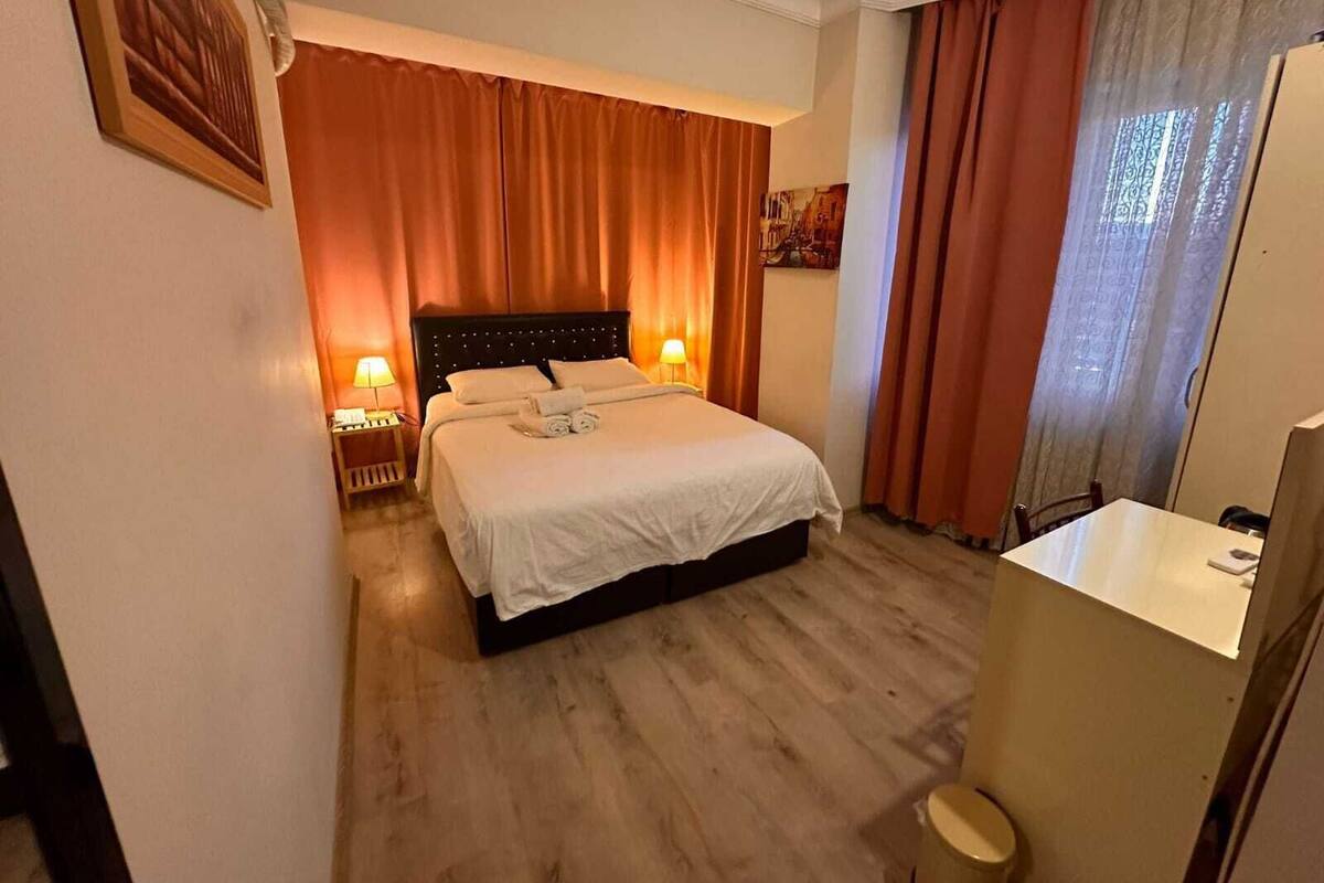 A hotel room with a bed, bedside lamps, a desk, and a window with curtains.