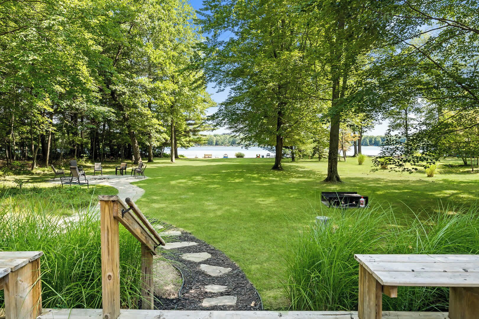 Un espace extérieur paisible, avec un sentier de pierres menant à une pelouse verdoyante, entouré d’arbres et bordé, au loin, par une étendue d’eau.