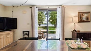 Un salon moderne doté d’un téléviseur à écran plat, d’un coin repas avec une table et des chaises, et offrant une vue sur un jardin grâce à une porte vitrée.