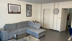 Un salon moderne avec un canapé d’angle gris, une petite table basse et une horloge murale.