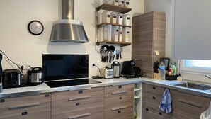 Une cuisine moderne dotée d’une hotte en acier inoxydable, d’un four encastré, d’une machine à café et de divers ustensiles et récipients rangés sur des étagères.