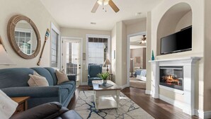 A living room with a fireplace, a television mounted above it, a blue sofa, and a ceiling fan.