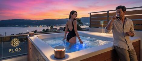 Una pareja en un jacuzzi con vista a un paisaje urbano al anochecer.