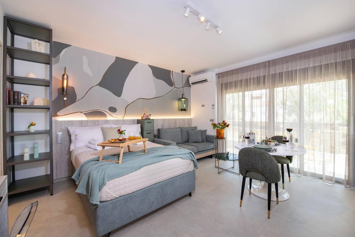 A modern bedroom with a bed, bedside table, and a dining area with a table and chairs.