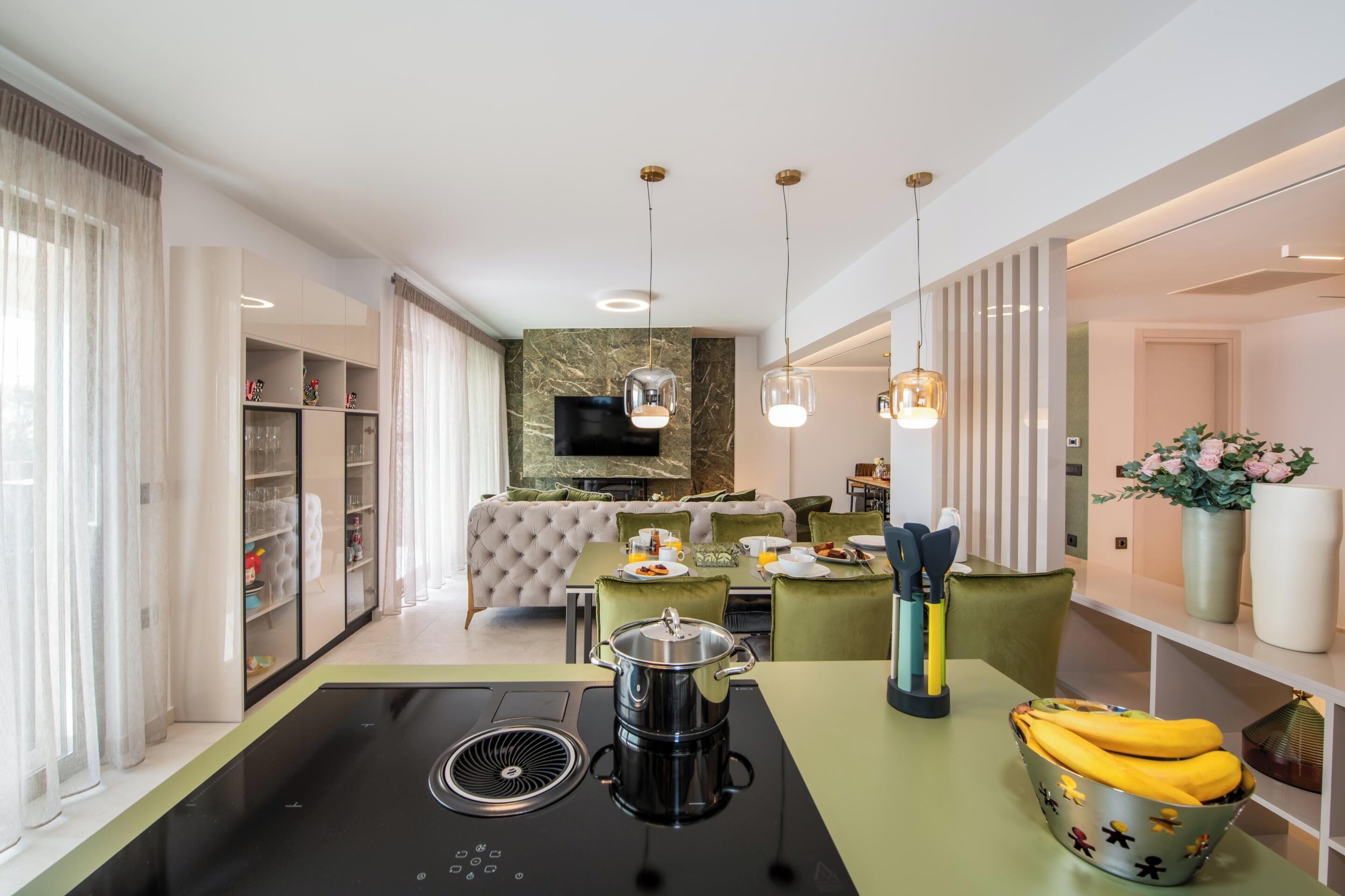 A modern kitchen with a built-in stove, a dining area with a table and chairs, and a living room with a sofa and a TV.