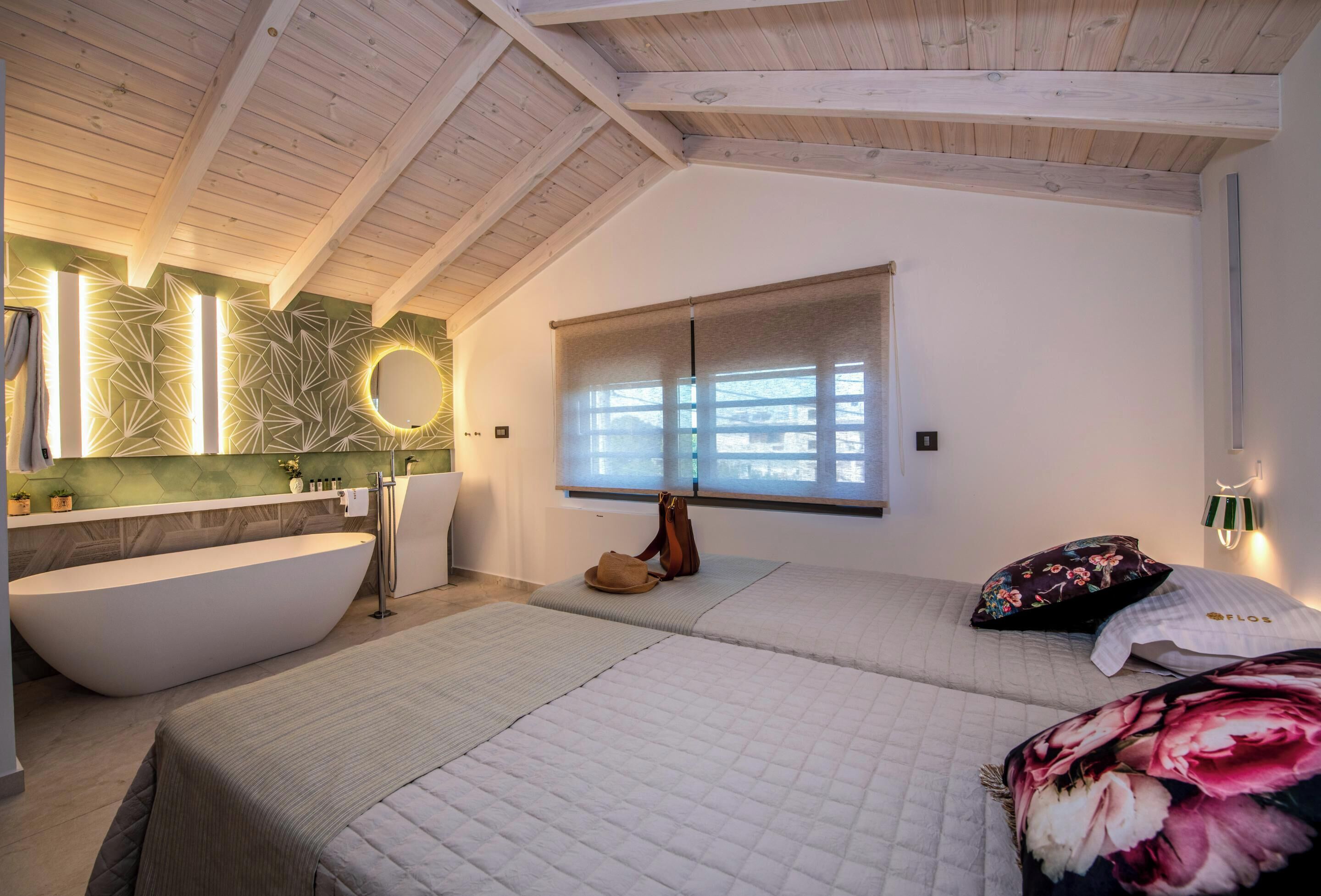 Un dormitorio moderno con una bañera grande, una cama con cubrecama floral y una ventana con vistas.