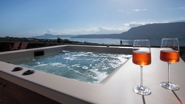 Een hottub met twee glazen wijn op een tafel, met uitzicht op een waterpartij en bergen.