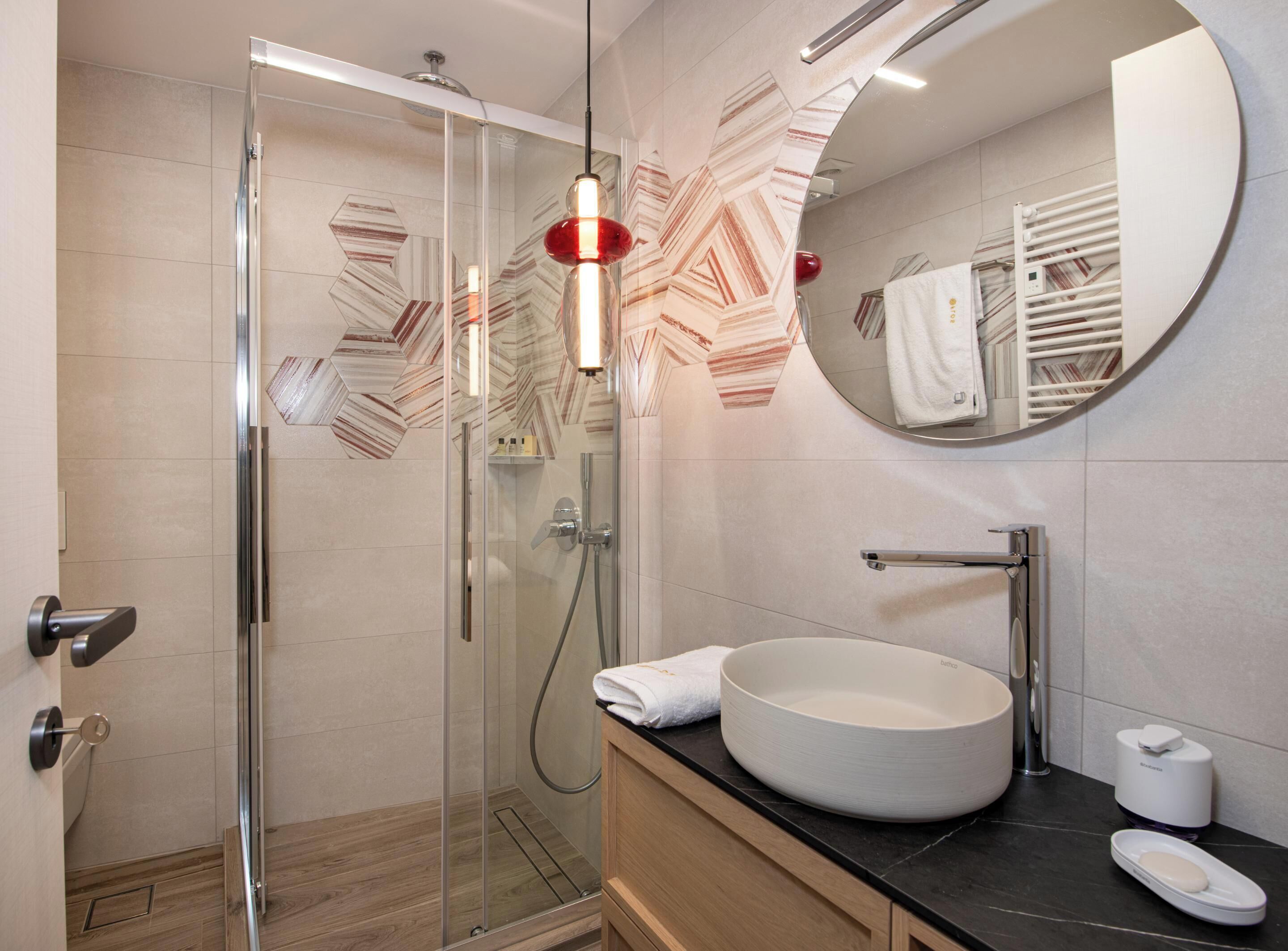 A modern bathroom with a glass-enclosed shower, a round sink, and a mirror with a geometric tile backsplash.