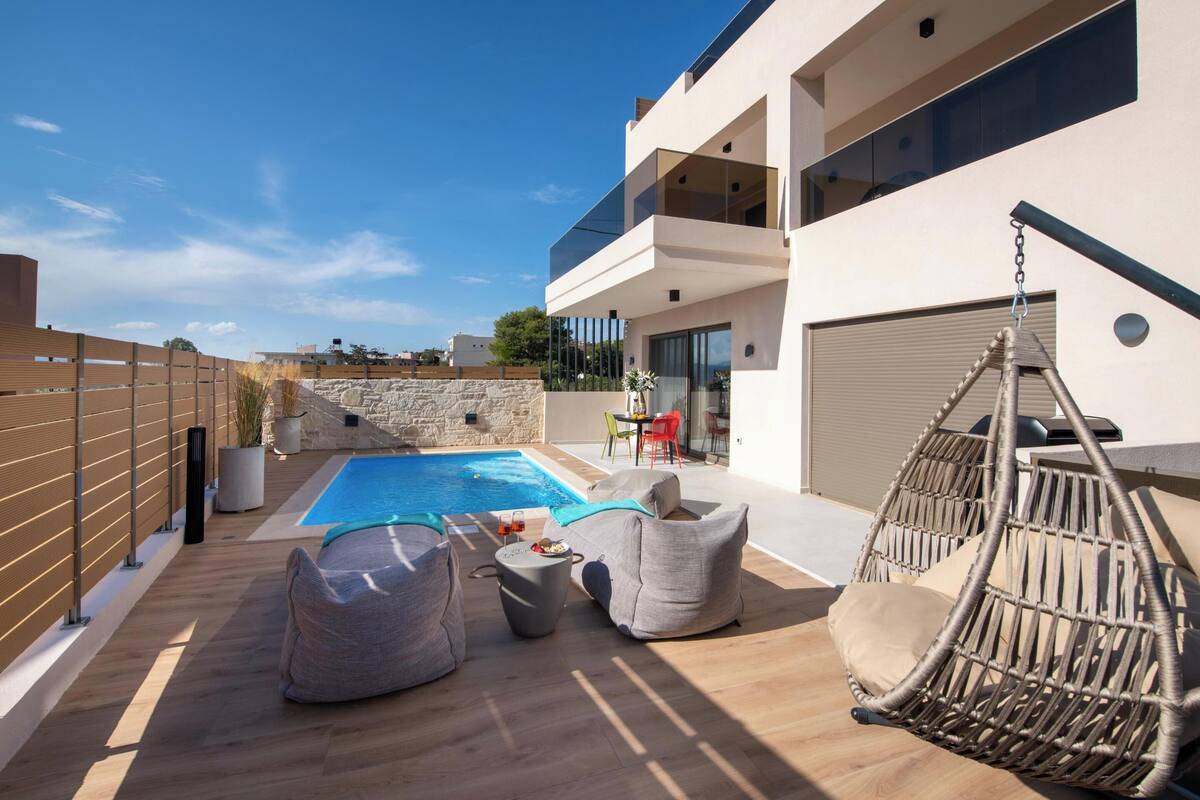 A modern outdoor pool area with lounge seating and a hanging chair.