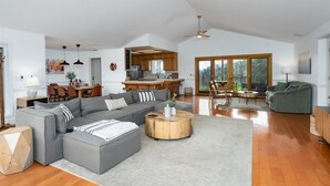 A spacious living area with a grey sectional sofa, a round wooden coffee table, and a dining area with a wooden table and chairs. - New! Big Sky Cabin at Yosemite w/ VIEWS, hot tub, firepit, and more! (Oakhurst)