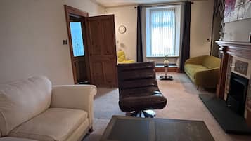 Una sala de estar con un sofá blanco, un sillón marrón, un sillón amarillo, una chimenea y una ventana con cortinas.