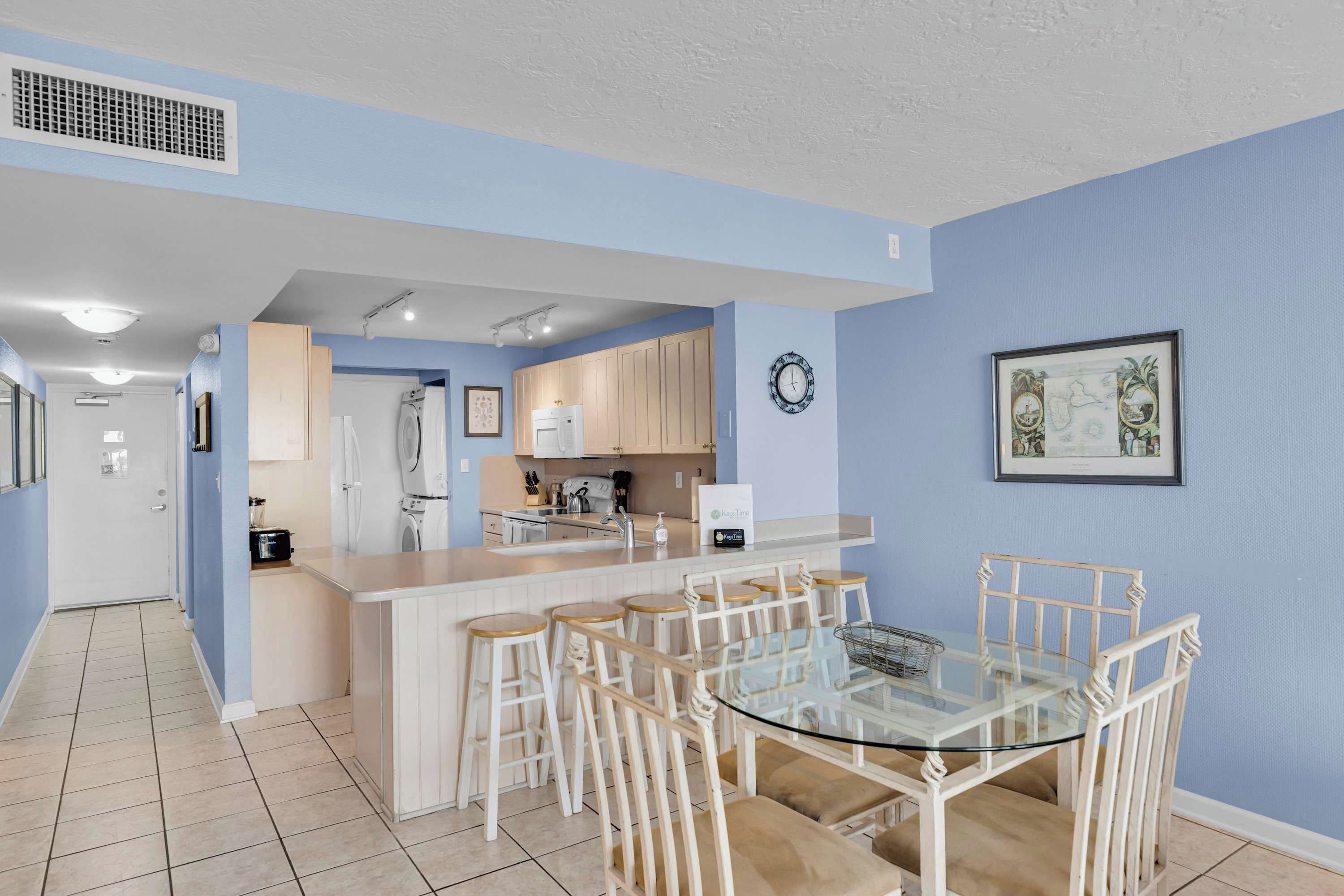 Una cocina moderna con una isla central, taburetes de bar y una mesa de comedor de vidrio.
