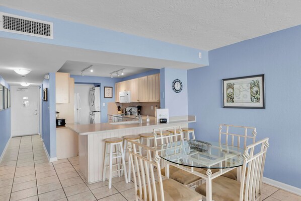 Una cocina moderna con una isla central, taburetes de bar y una mesa de comedor de vidrio.