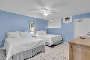A bedroom with two single beds, a ceiling fan, a window with blinds, and a door with a handle.