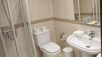Un baño con cabina de ducha de vidrio, inodoro, lavamanos y espejo.