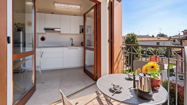 A balcony with a table, a potted plant, and a view of the neighborhood. - Garda Girasole quiet three-room apartment near the lake with private parking (Desenzano del Garda)