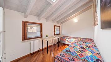 A small room with a sloped ceiling, a bed with a colorful patterned bedspread, a desk with a chair, and a window with a curtain.