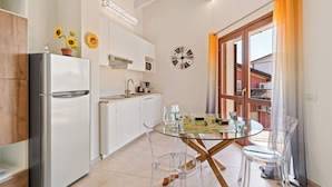 A modern kitchen with a refrigerator, white cabinets, a glass dining table with chairs, a clock, and a window with curtains. - Garda Girasole quiet three-room apartment near the lake with private parking (Desenzano del Garda)
