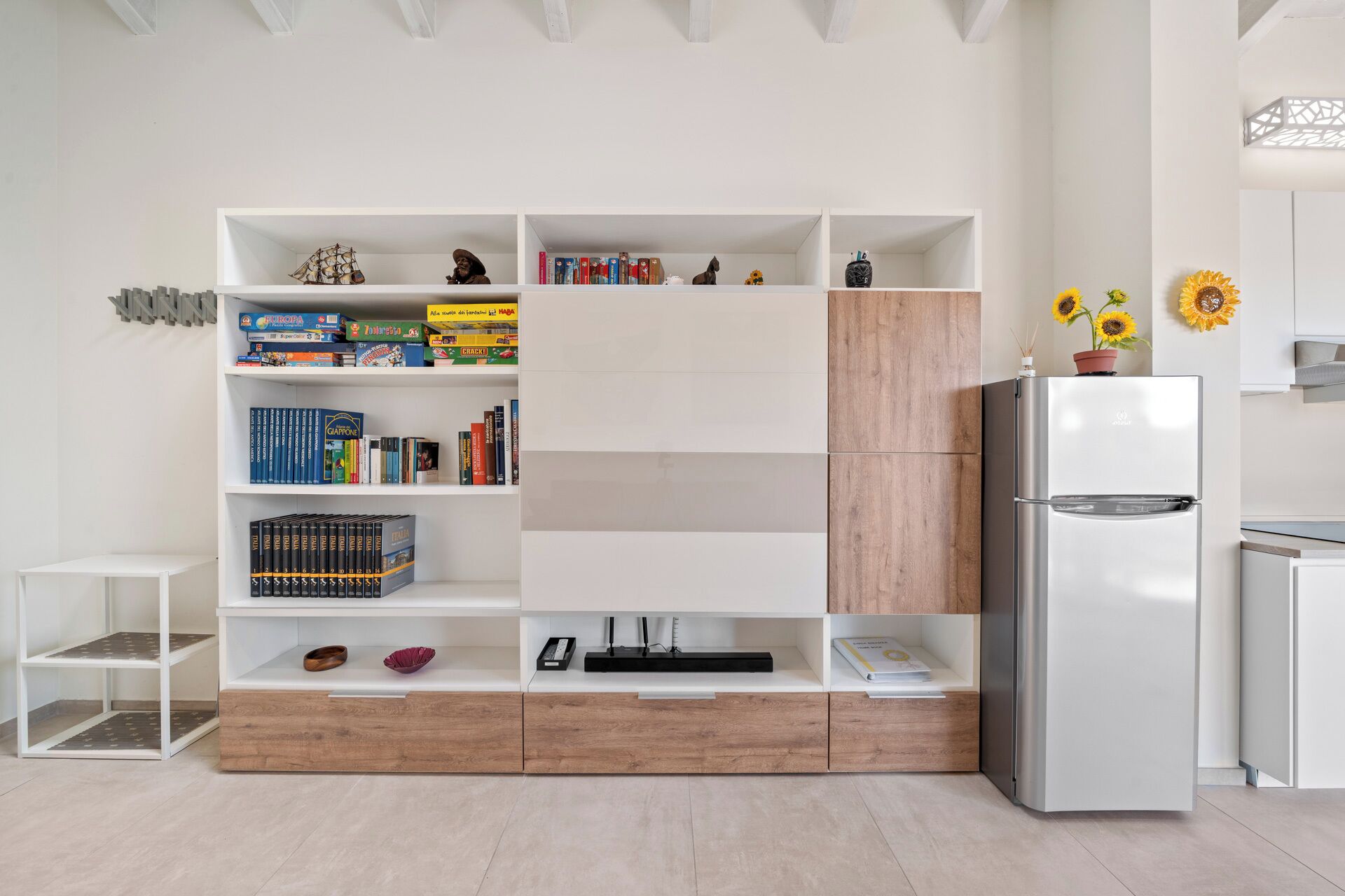 Una cucina moderna con mobili bianchi, un armadio in legno a incasso e un frigorifero in acciaio inossidabile.