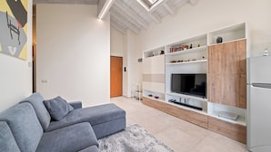 A modern living room with a grey sectional sofa, a built-in TV, and a wooden cabinet. - Garda Girasole quiet three-room apartment near the lake with private parking (Desenzano del Garda)