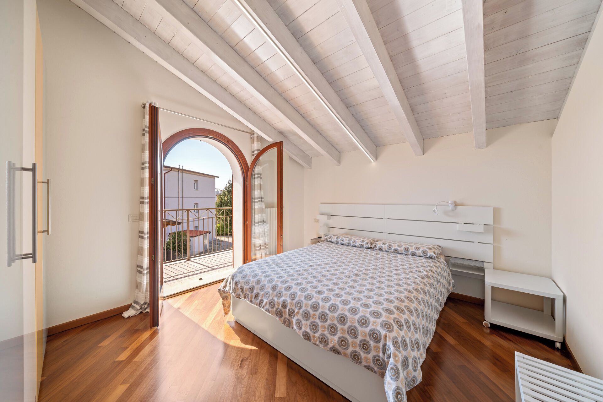 Una camera da letto con un letto, un comodino, una finestra e un arco che dà su un balcone esterno.