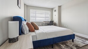 A bedroom with a bed, bedside table, lamp, and a desk with a chair. - Legacy at Imperial Village 1014 I 2 Bed 2 Bath (Ric hmond)