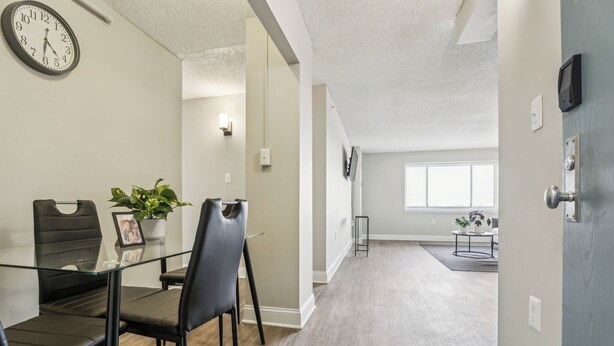 A modern hotel room with a glass dining table, black chairs, a potted plant, a clock, and a view of the hallway. - Legacy at Imperial Village 1014 I 2 Bed 2 Bath (Ric hmond)