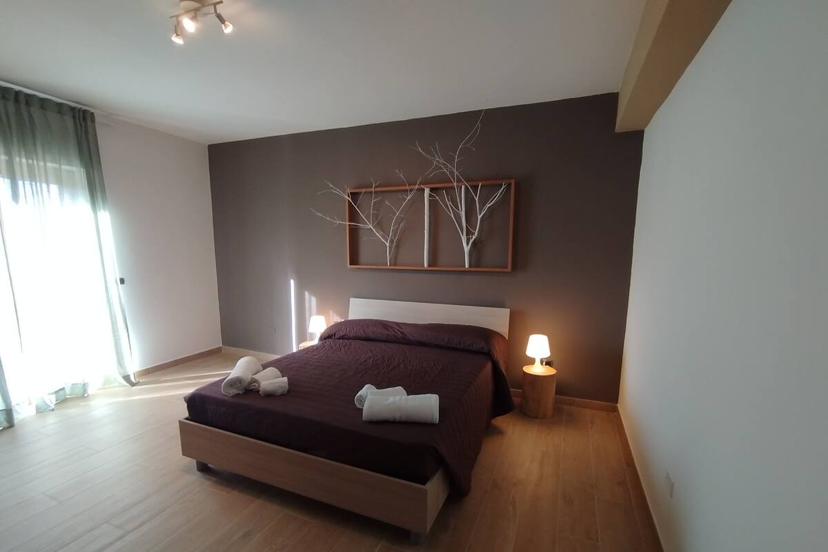 A modern bedroom with a large bed, two bedside lamps, and a wall-mounted artwork.