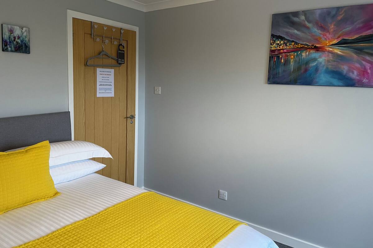 A hotel room with a bed, a door with a sign, and a painting on the wall.