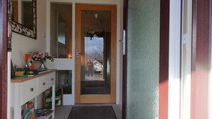 Una puerta de madera con un panel de vidrio, un felpudo y un estante con libros y un jarrón de flores.