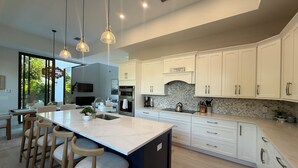 Une cuisine moderne avec des meubles blancs, un grand îlot central doté de tabourets et des luminaires suspendus.