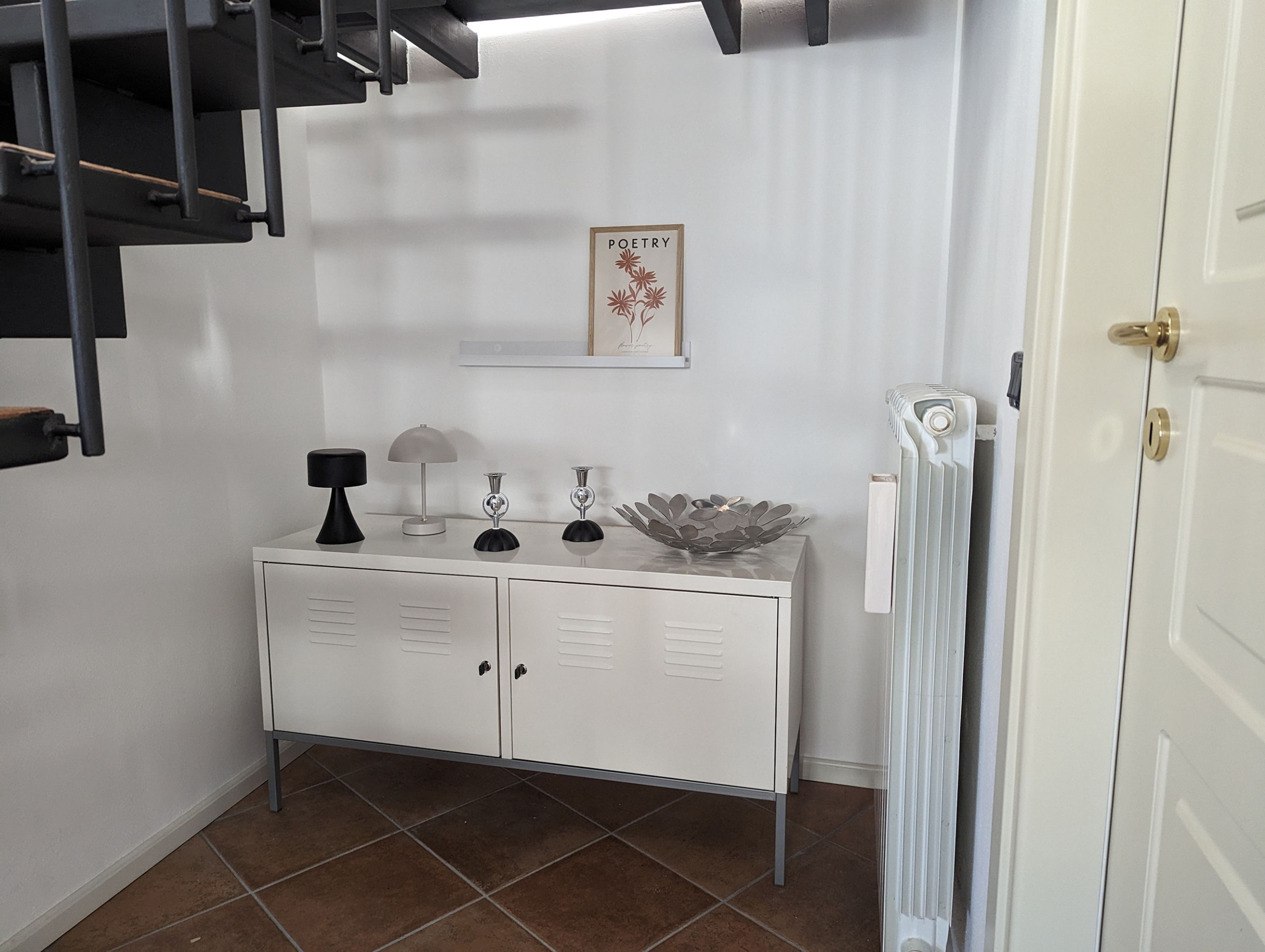 Un meuble blanc à deux portes, une lampe noire, une lampe argentée et un bol décoratif posé sur le dessus.