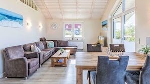 A spacious living room with a wooden ceiling, a large window, and a view of the outside.