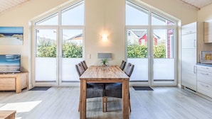 A spacious dining area with a wooden table and chairs, large windows, and a view of the outside.