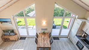 A modern kitchen with a dining area, large windows, and a TV on a wooden stand.