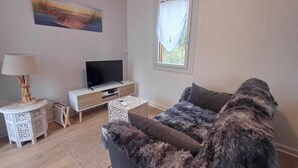 Uma sala de estar com um sofá, uma televisão, um abajur e um quadro na parede.
