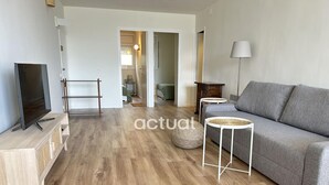 A modern living room with a grey sofa, a television on a wooden stand, and a lamp. - Charming apartment with pool near the beach in Platja d'Aro (Platja d'Aro)