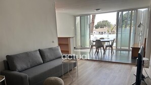A modern living room with a grey sofa, a round ottoman, and a dining area with a table and chairs. - Charming apartment with pool near the beach in Platja d'Aro (Platja d'Aro)