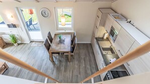 A modern kitchen with wooden cabinets, a dining area with a table and chairs, and a view of the outdoors through large windows. - Lovely apartment in villa for 2 people with WIFI, TV and terrace (Dagebüll)