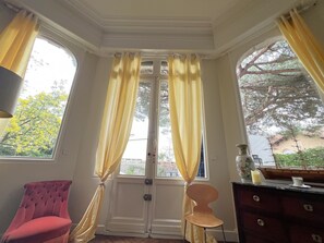 A room with a large bay window, a red chair, a wooden cabinet, and a vase on the windowsill. - Arcachon: Apartment 8 pers, near beach, garden, parking, wifi (Arcachon)