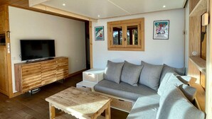 Un soggiorno moderno con soffitto in legno, un divano grigio, un tavolino in legno e un televisore su un mobile in legno.