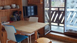 A wooden interior with a dining table, chairs, and a TV. Shelves above the table hold dishes and glasses. - Cozy apartment with balcony and parking in Chamonix, near the center (Chamonix-Mont-Blanc)