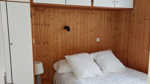 A bedroom with a wooden headboard, a bed with white bedding, a bedside table with a lamp, and a wardrobe with white doors. - Cozy apartment with balcony and parking in Chamonix, near the center (Chamonix-Mont-Blanc)