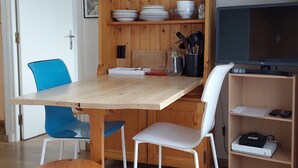 A compact living space with a wooden dining table, two chairs, a television, and a shelf with kitchenware. - Cozy apartment with balcony and parking in Chamonix, near the center (Chamonix-Mont-Blanc)