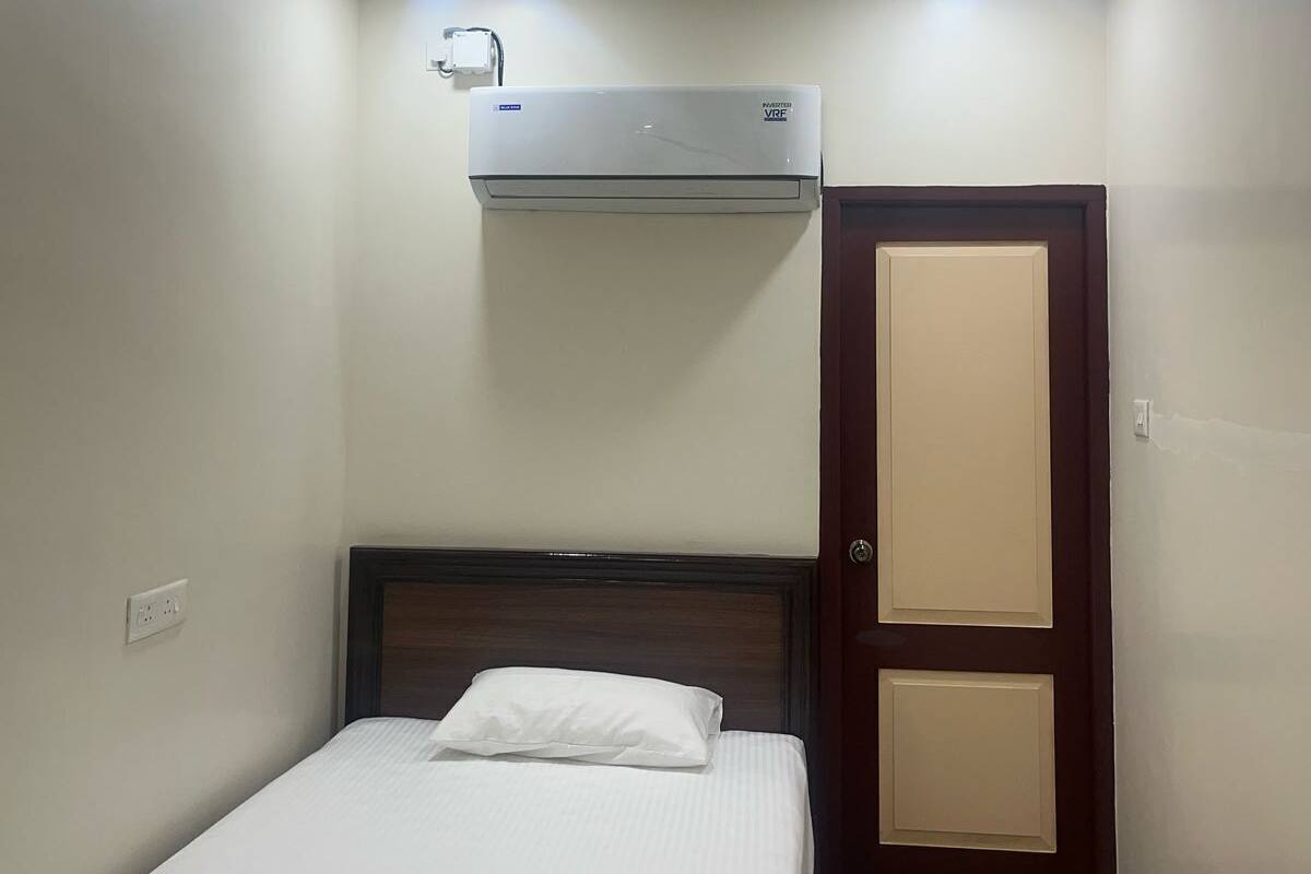 Una habitación de hotel con una cama individual, ventilador de techo, equipo de aire acondicionado y una puerta.