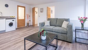 A modern living room with a grey sofa, a coffee table, and a washing machine in the background.