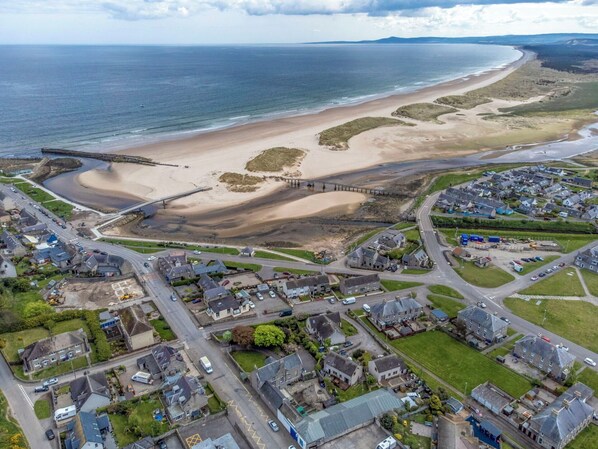 An aerial view of a coastal town with a beach, a bridge, and residential areas.